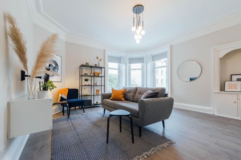 Bright living room with grey sofa, yellow armchair, wooden floors and large windows