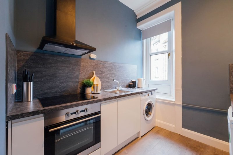 Modern kitchen with white cabinetry, dark countertop, integrated appliances and window