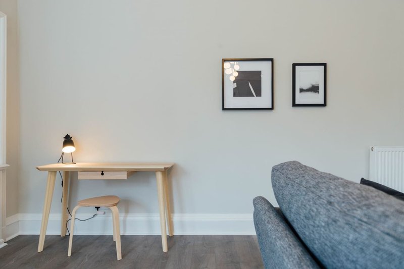 Modern studio with wooden desk, chair, lamp, and gray upholstered sofa