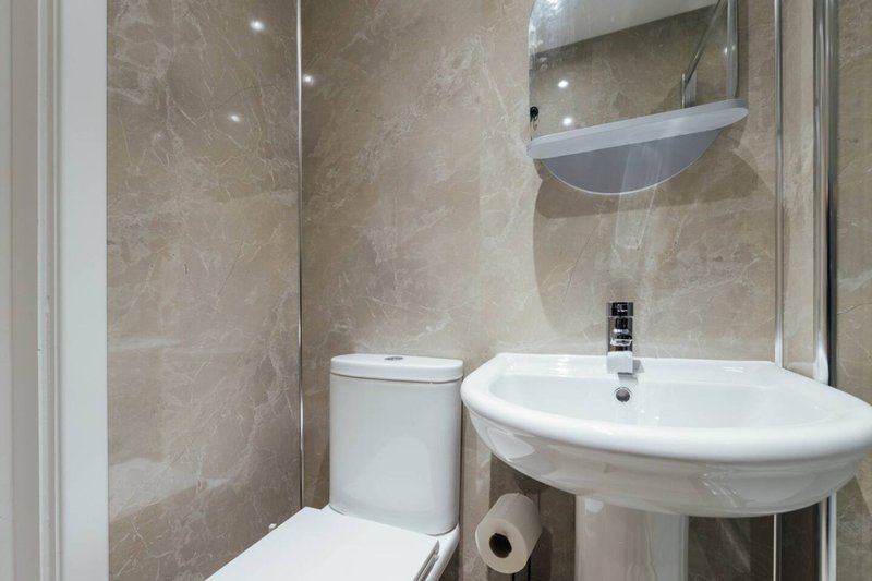 Modern bathroom with white sink, toilet, shower enclosure and beige tile walls