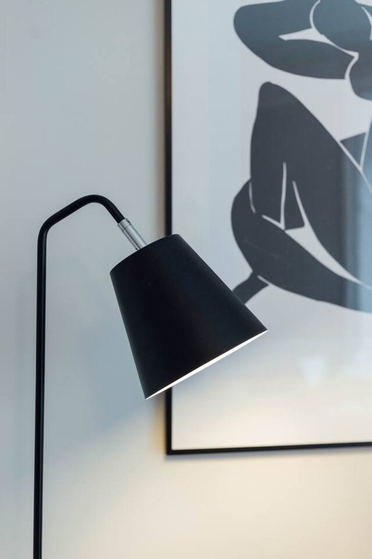 Black arc floor lamp next to framed abstract artwork on white wall