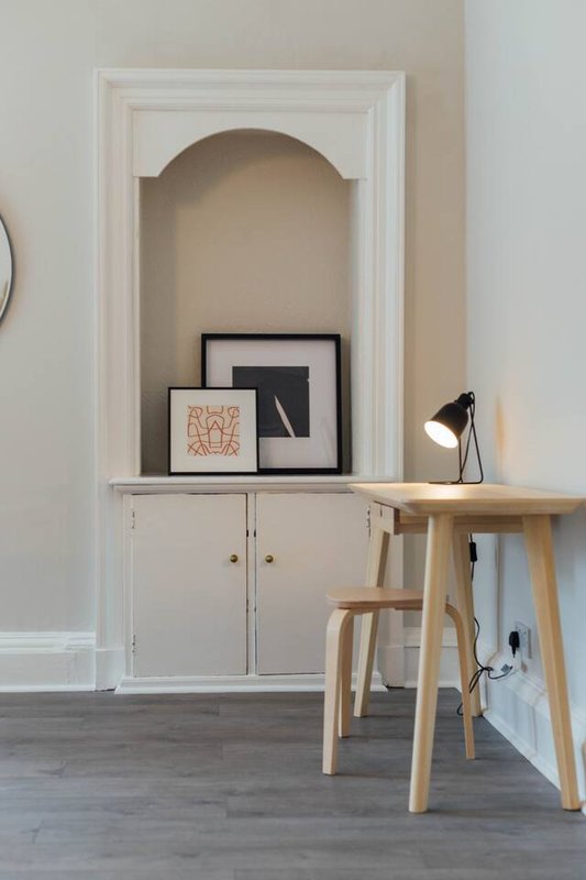 Modern workspace with wooden desk, chair, black desk lamp and built-in wall niche with artwork
