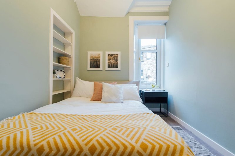 Bright bedroom with yellow geometric bedspread, white built-in shelving, and window with natural light