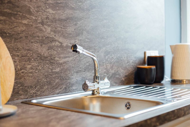 Kitchen sink with chrome faucet, backsplash, and decorative items on counter