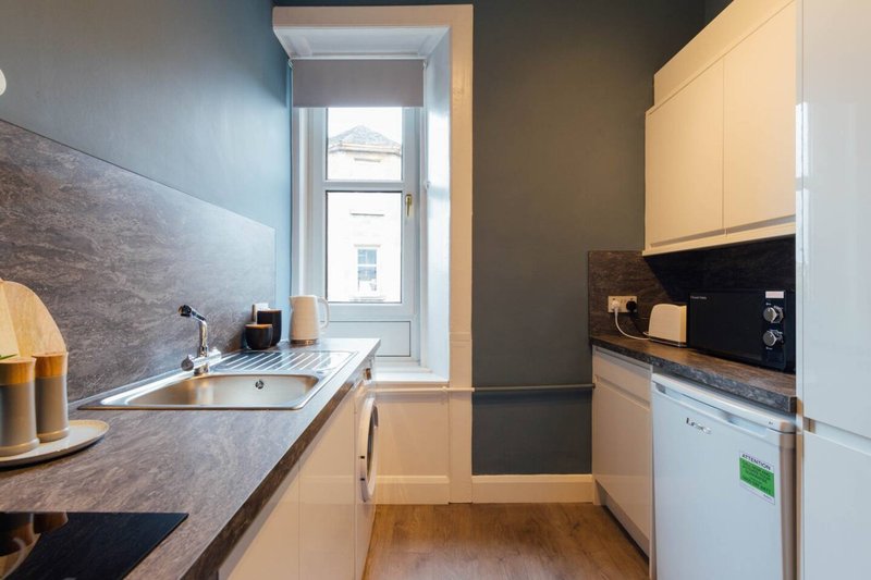 Modern galley kitchen with white cabinetry, dark countertops, window and appliances