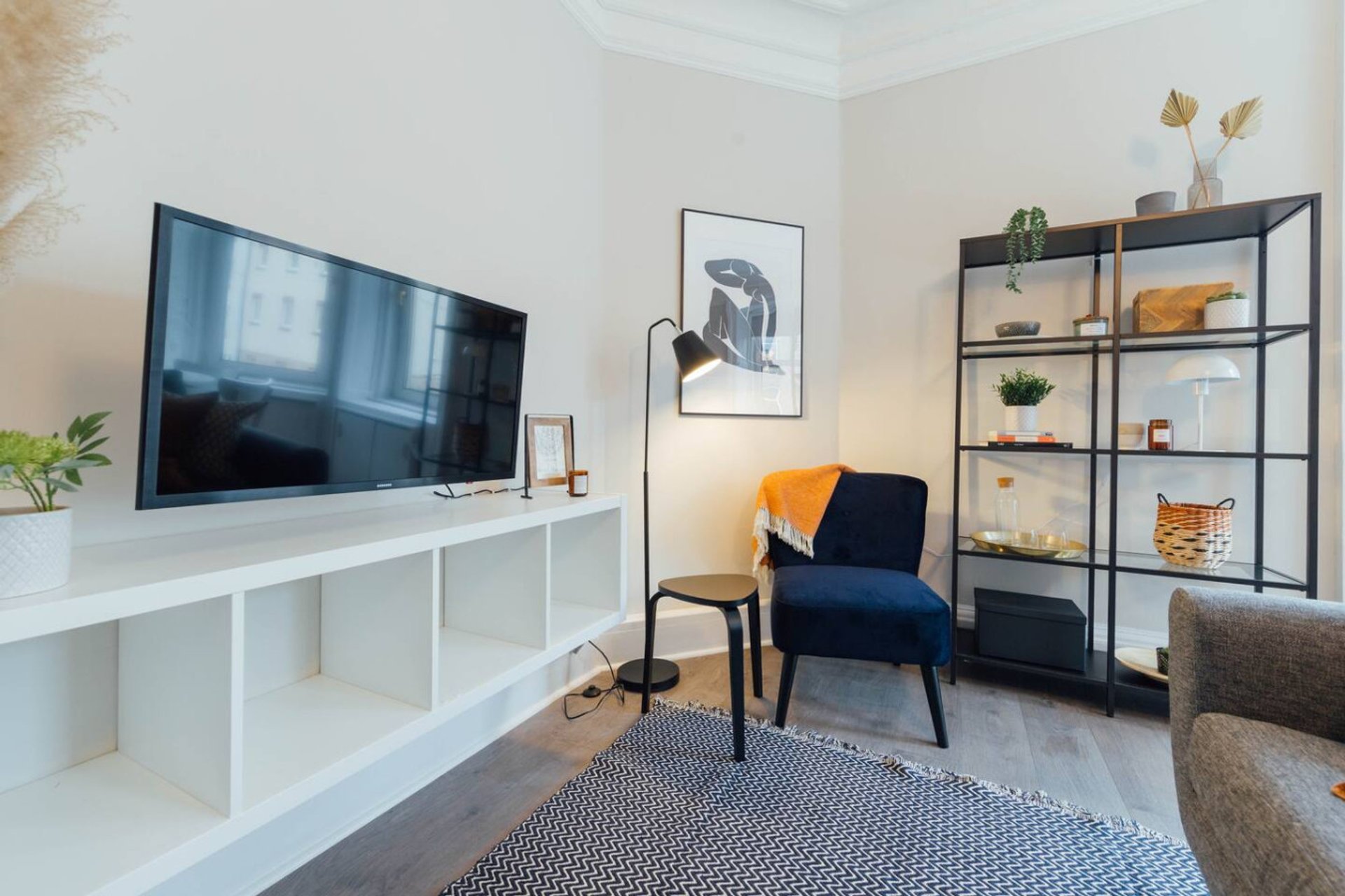 Modern living room with TV on white media unit, blue armchair, shelving unit and neutral decor