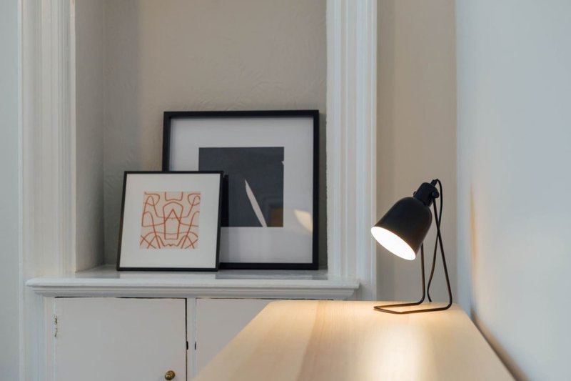 Floating shelf with framed artwork, black desk lamp, and minimalist wall decor