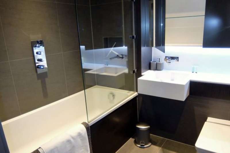Modern bathroom with walk-in shower, dual sink vanity, dark tile walls and white fixtures