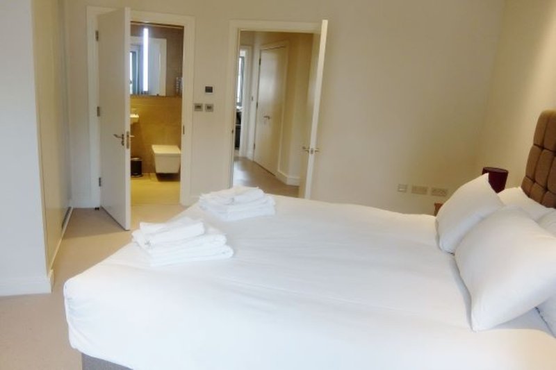 Bright bedroom with double bed, white bedding, pillows, and open doorways to ensuite bathroom