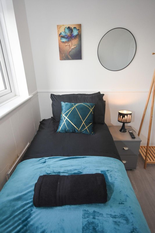Modern bedroom with single bed, blue bedding, dark cushion, round mirror and wall art