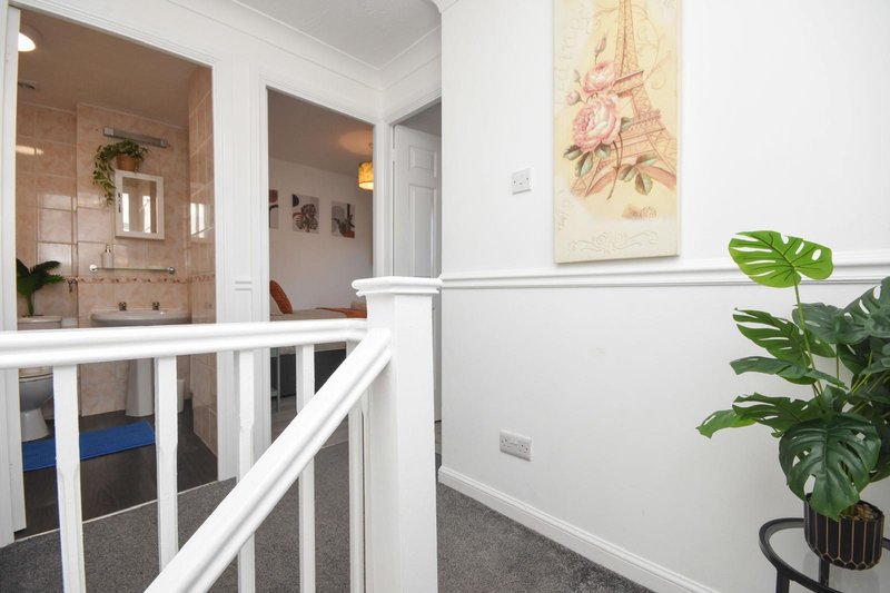 Bright hallway with white railing, potted plant, framed floral art, and bathroom visible