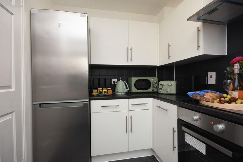 Modern kitchen with white cabinets, stainless steel fridge, black countertops and appliances