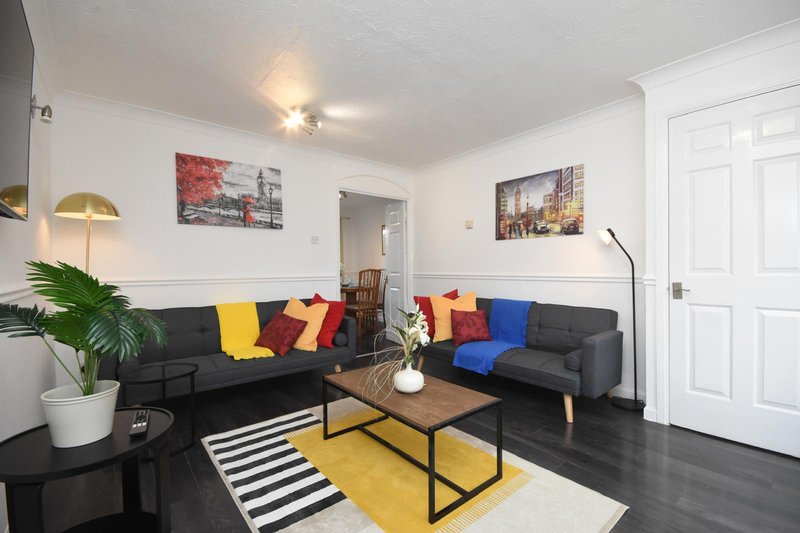 Modern living room with black sofas, colorful cushions, wooden coffee table and framed wall art