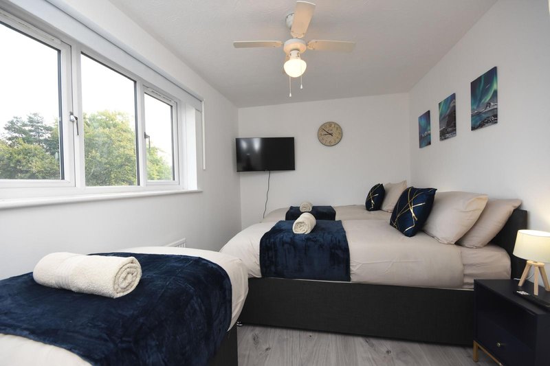 Bright bedroom with two single beds, navy bedding, wall-mounted TV, and large windows