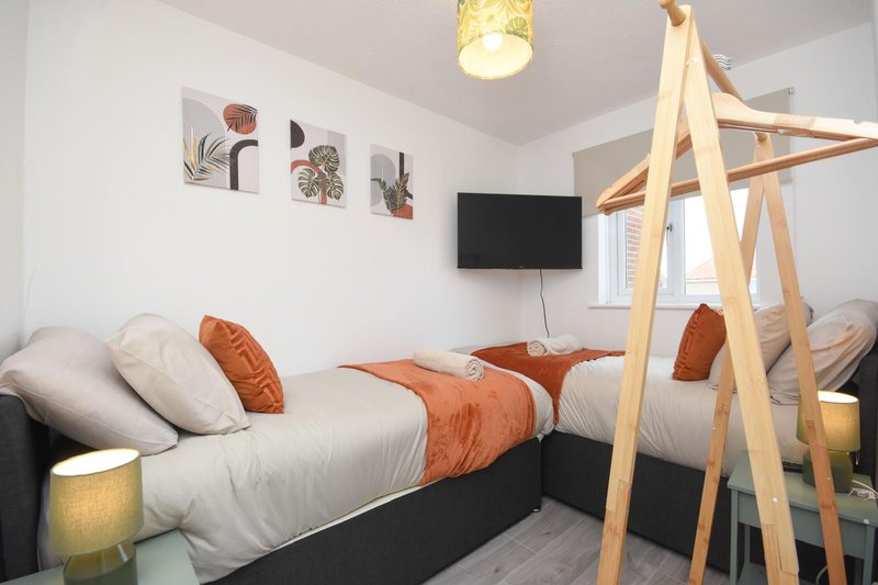Bedroom with single bed, orange cushions, wooden canopy frame and wall-mounted TV