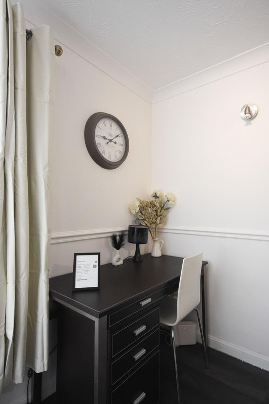 Home office nook with black desk, chair, wall clock, dried flowers, and cream curtains