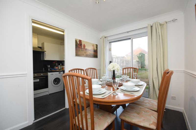 Dining room with wooden table, chairs, kitchen area visible, and glass doors to garden