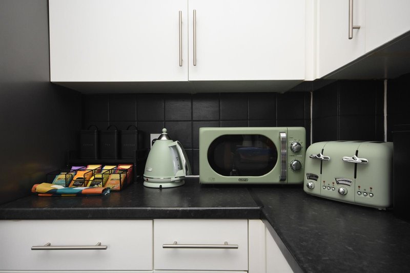 Modern kitchen with white cabinets, black countertop, vintage retro appliances and tea kettles