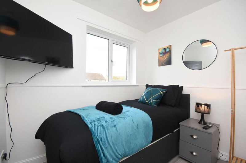 Modern bedroom with black bed, blue bedding, wall-mounted TV, round mirror and window