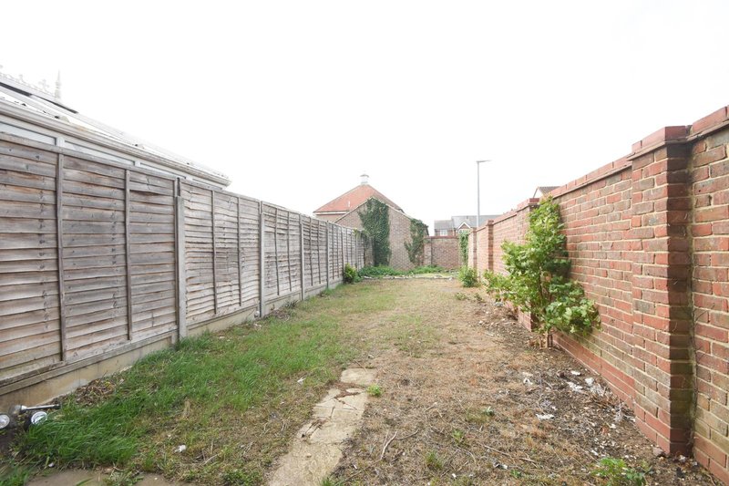 Side garden area with wooden fence, brick wall, grass and gravel pathway