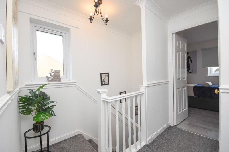 Bright hallway with white staircase railing, potted plant on side table, and bedroom doorway