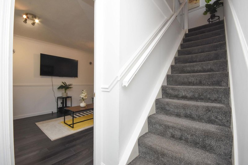 Interior staircase with gray carpet and white railings, view of living room with TV and furniture