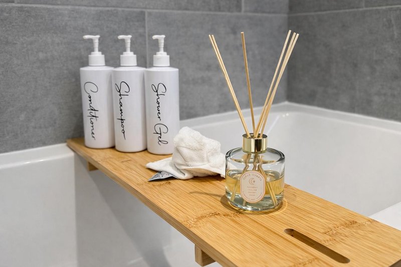 Bathroom shelf with toiletries, diffuser, tissues and decorative items above bathtub