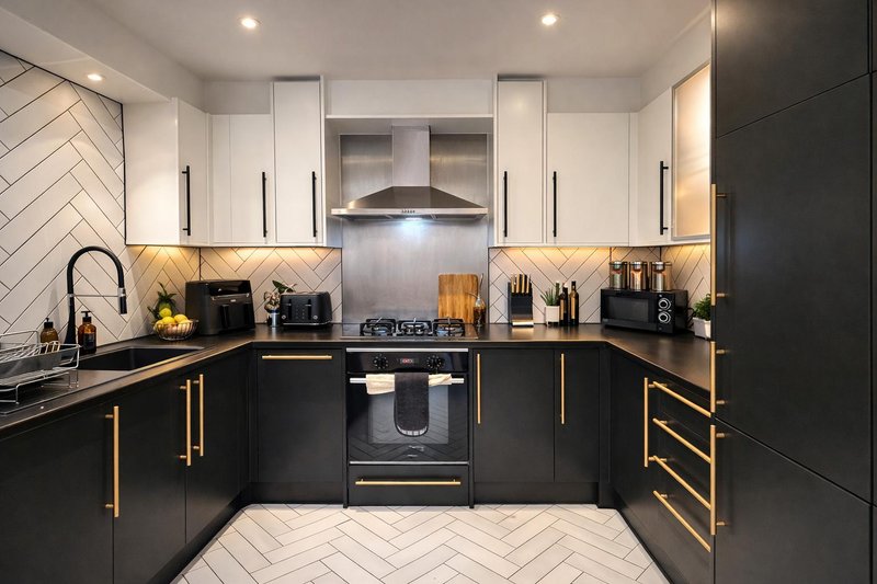 Modern kitchen with black cabinetry, gold handles, white herringbone backsplash and flooring