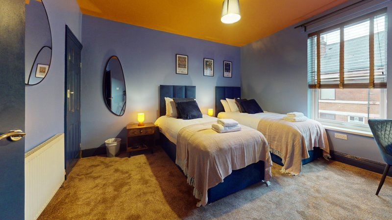 Bedroom with two single beds, yellow bedding, blue headboards, and large windows