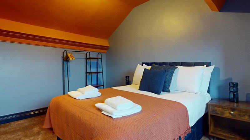 Bright bedroom with double bed, orange throw, white pillows, blue headboard and wooden nightstand