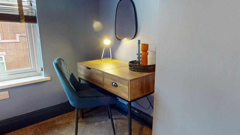 Wooden desk with drawer, blue chair, mirror and lamp in bedroom corner