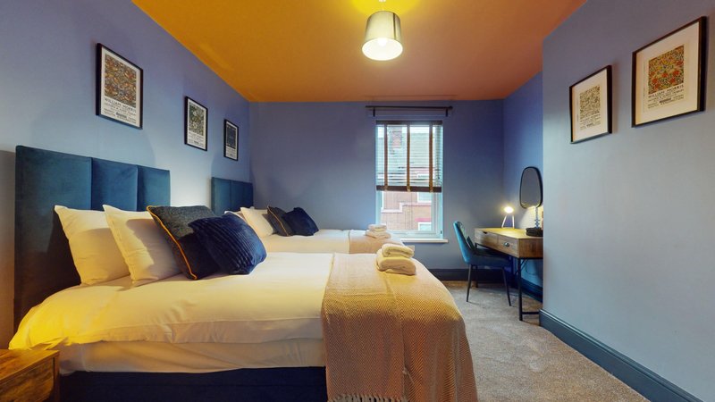 Bright bedroom with yellow bedding, blue walls, framed artwork, and desk area by window