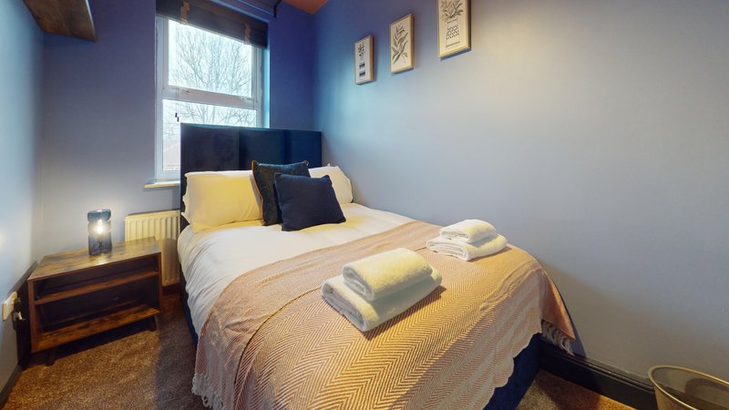Compact bedroom with double bed, yellow bedding, navy headboard, and window