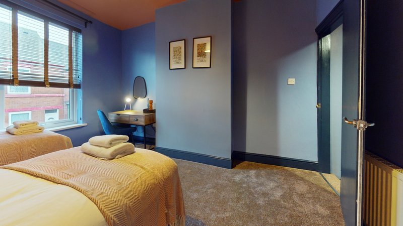 Bedroom with two single beds, yellow bedding, desk with lamp, and blue walls
