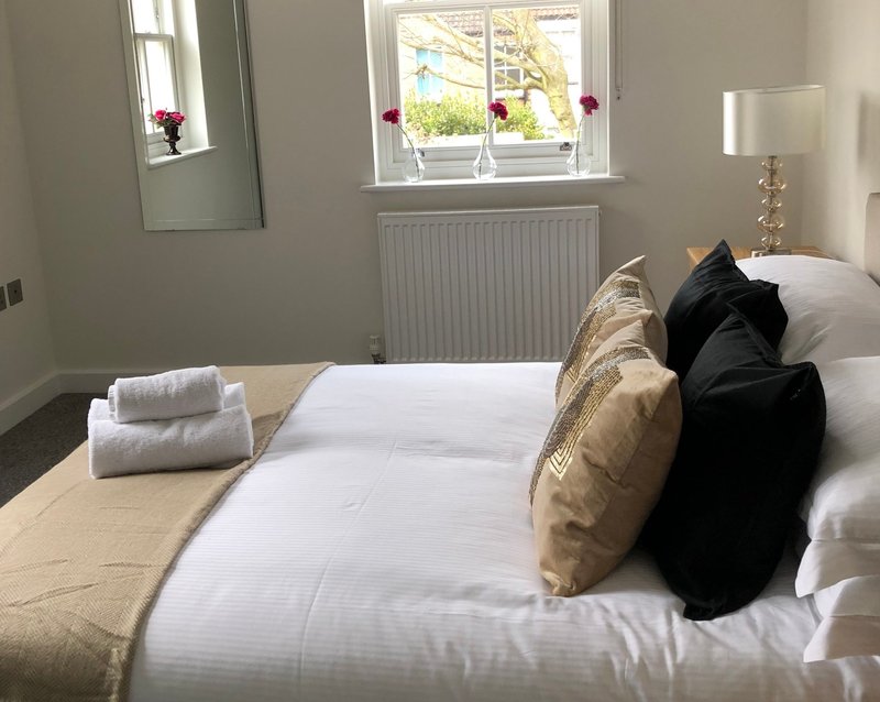 Bright bedroom with double bed, white pillows, decorative cushions, mirror and window with garden view