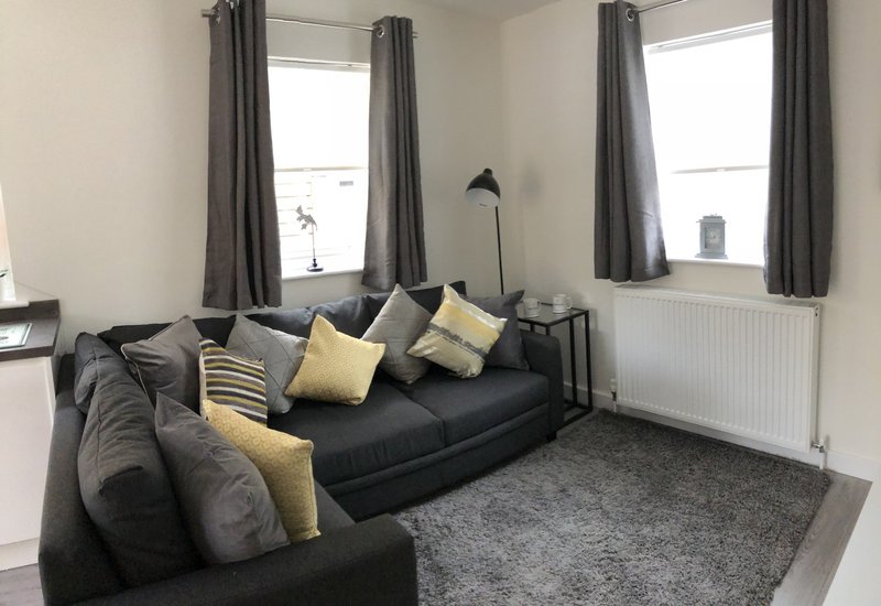 Bright living room with black corner sofa, yellow cushions, grey carpet and large windows