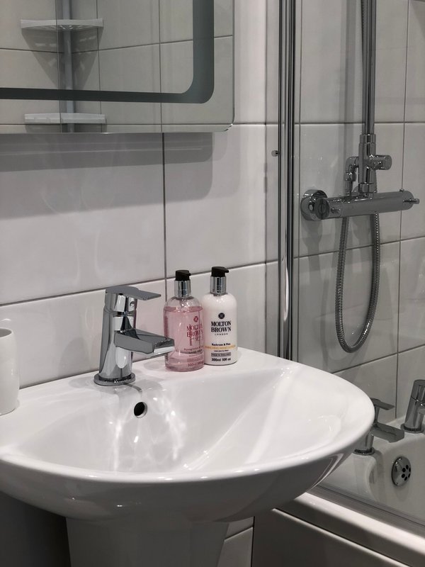 Modern bathroom with round white sink, chrome faucet, toiletries, and glass shower enclosure