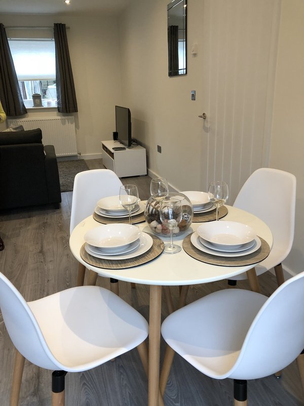 Dining area with round white table, four white chairs, place settings and water pitcher