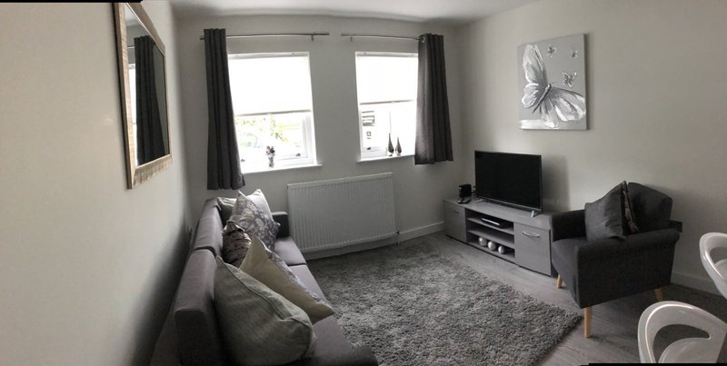 Living room with grey sofa, TV unit, armchair, grey rug and window with dark curtains
