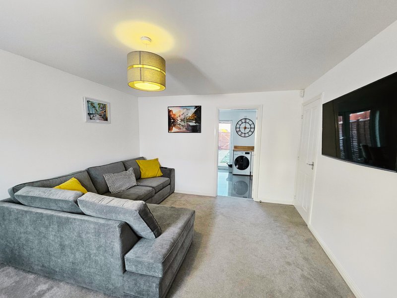 Modern living room with grey sofa, yellow cushions, ceiling light, wall-mounted TV and open doorway