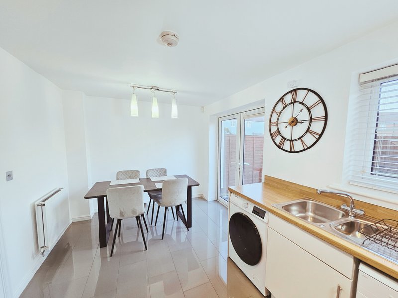 Modern kitchen and dining area with wooden table, cream chairs, stainless steel appliances and wall clock