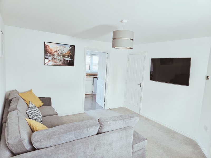 Modern living room with grey L-shaped sofa, yellow cushions, wall-mounted TV and framed artwork