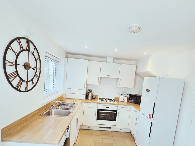 Modern kitchen with white cabinetry, wooden worktops, stainless steel appliances and large wall clock