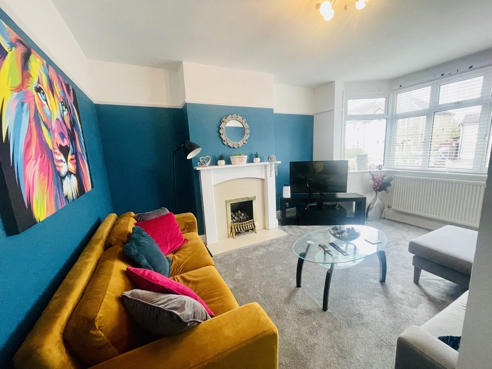 Modern living room with mustard-yellow sofa, teal accent wall, fireplace, and large windows