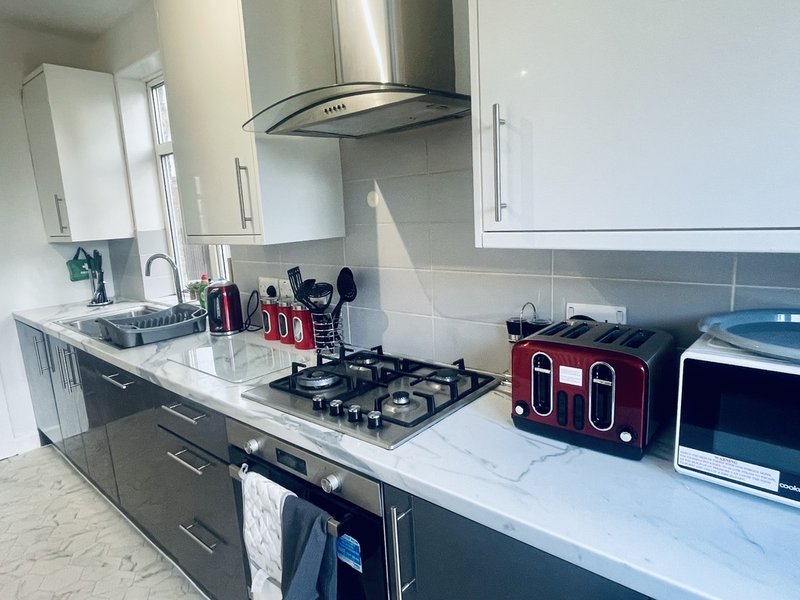 Modern kitchen with white countertops, black gas hob, red kettle and toaster, stainless steel hood