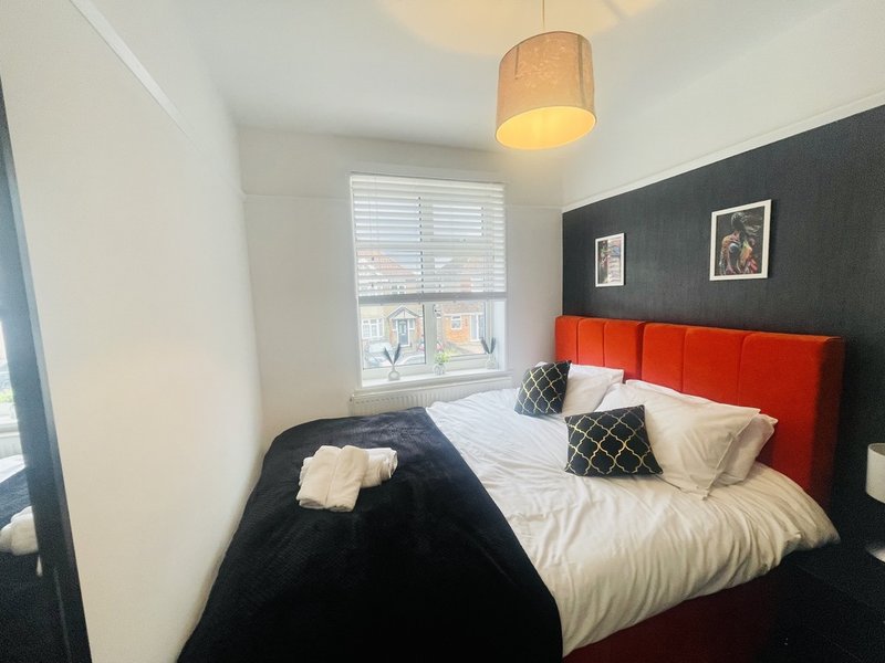 Bedroom with red headboard, white bedding, dark accent wall, pendant lamp and window with shutters