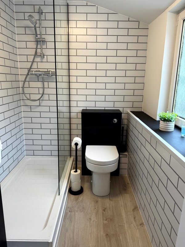 Modern bathroom with white subway tiles, walk-in shower, toilet, and window with windowsill plant