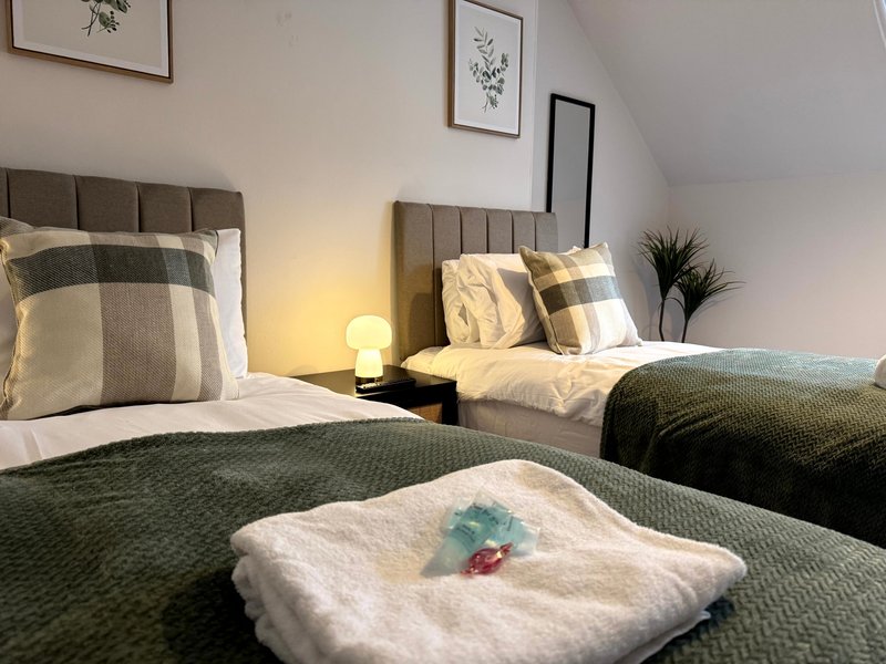 Twin bedroom with grey upholstered headboards, patterned bedding, warm lighting, and framed wall art