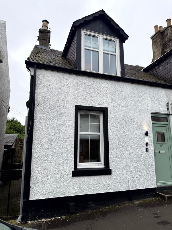 White-rendered cottage exterior with black roof dormer, two windows and green door