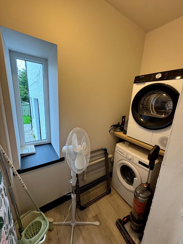 Utility room with stacked washing machine and dryer, portable fan, and door to garden